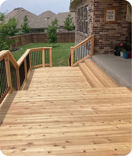A newly built wooden deck with black metal railings leads down from a brick house to a grassy fenced backyard. Several potted plants sit near the door, and a sign reads Porch Happy Place—perfect inspiration for new home decks in San Antonio, Texas.